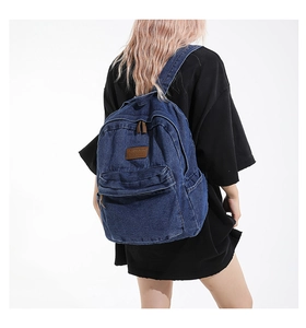 Detail of vintage navy denim backpack with brown leather patch and dual metal zippers