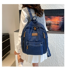 Close-up of durable dark blue denim backpack featuring leather zipper pulls and brand tag