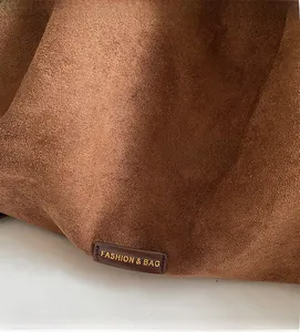 Close-up of brown suede tote bag featuring a leather fashion label with gold text details