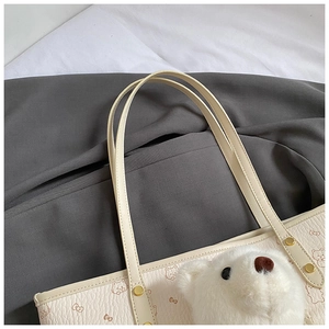 Detail of beige faux leather tote with cat print and plush bear head charm attachment