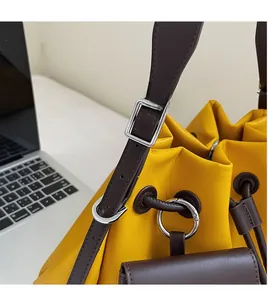 Detail of yellow drawstring bucket bag with smooth brown leather strap and silver buckle