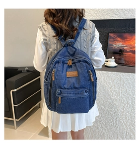 Detail view of a vintage dark blue denim backpack with brown leather logo patch on rear