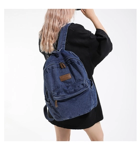 Detailed back view of a washed blue denim backpack with brown leather accents
