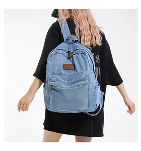 Back view of a light blue denim backpack with leather buckles on a model