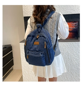 Detail view of deep blue denim backpack with brown leather logo patch on adjustable straps