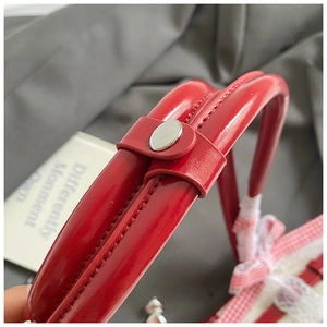 Détail du sac rouge en cuir verni avec boucle en métal, dentelle et doublure à carreaux