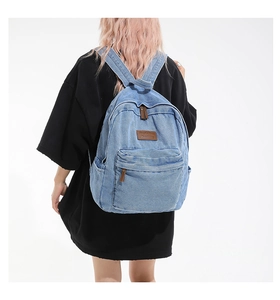 Detail of light blue denim backpack showing side pocket and brown leather logo patch