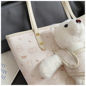 Detailed shot of cream tote bag featuring cartoon cat print and plush bear charm