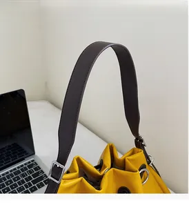 Close-up of yellow bucket bag showing lychee grain texture and brown wide handle strap
