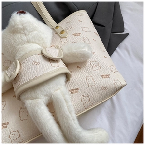 Detail of cream leather tote bag with cat patterns and soft plush bear charm accessory