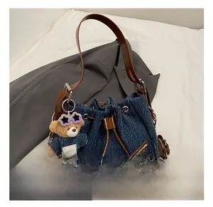 Detail of denim bucket bag with brown leather handles and a plush bear pendant charm