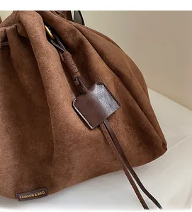 Close-up of brown suede drawstring bucket bag with decorative tag and fashion logo