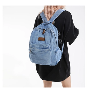 Detail of vintage blue denim backpack with brown leather logo patch on street style model