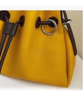 Close-up of soft yellow leather bucket bag with brown drawstring and silver metal hardware