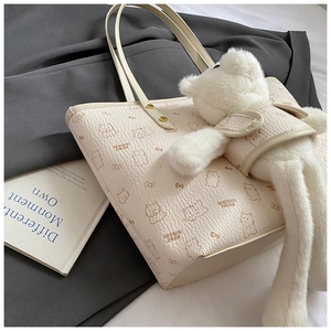 Cream tote bag with brown cartoon cats, brand lettering, and white plush bear charm