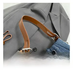 Detail of dark blue denim tote with brown leather handles and silver metal buckle