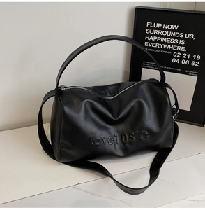 Detail of black leather tote bag featuring embossed lettering and adjustable strap