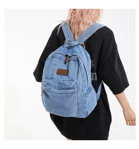 Detail of light blue denim backpack showing vintage wash fabric and leather brand tag