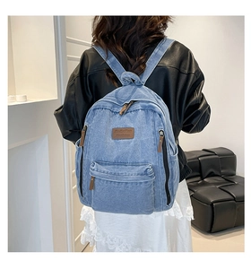 Rear view of a blue denim backpack with leather patch worn with a black leather jacket