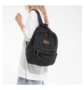 Side view of a black washed denim backpack with leather patch and zipper pockets
