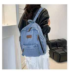 Detail of light blue denim backpack with brown leather accents shown on a model
