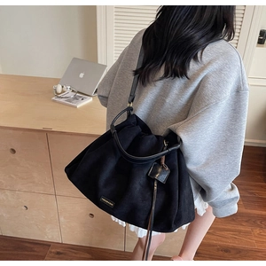 Detail of black suede tote bag with metal label and leather tag in an office setting