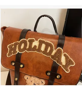 Detail of vintage brown leather backpack with HOLIDAY plush letters and teddy bear patch