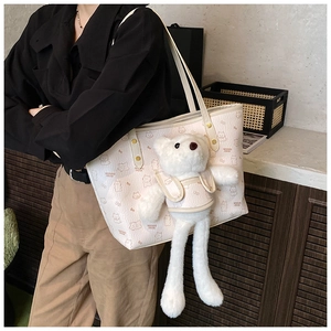 Detail of cream tote bag with bear patterns and a plush charm shown on a model