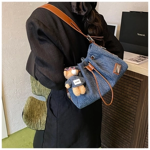Detail of denim bucket bag showing brown leather drawstring and cute bear plush charm