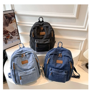 Three casual denim backpacks in black, light blue, and dark blue with leather logo labels