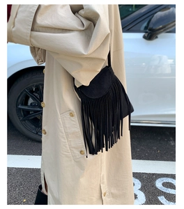 Outdoor street style view of a black fringed crossbody bag with soft suede texture