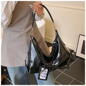 Detail of glossy black patent leather hobo bag with braided chain and decorative tag