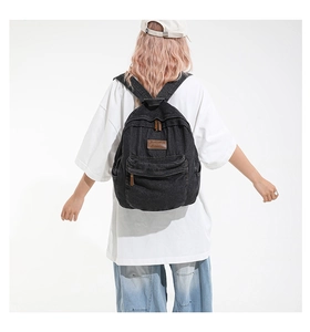 Close-up of black denim backpack featuring vintage brown leather logo and metal zipper