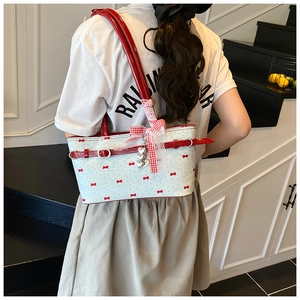 Détail d'un sac à bandoulière blanc avec nœuds rouges et breloques porté par mannequin