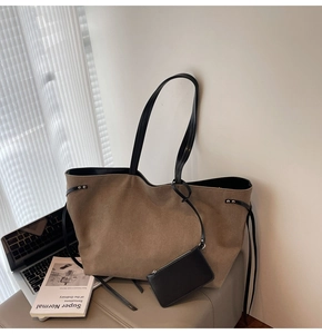 Borsa tote in camoscio marrone con manici neri accanto a laptop e libri in luce naturale