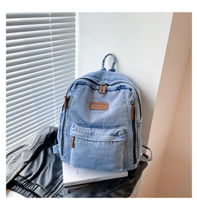 Detailed close-up of light blue denim backpack with brown leather tag and premium zipper
