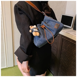 Detail of blue denim tote bag with drawstring, brown strap, and a teddy bear charm
