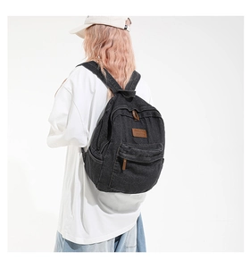 Detail of vintage black denim backpack on model showing canvas texture and zipper pockets