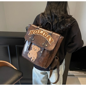 Detail of vintage brown leather backpack with plush HOLIDAY patch and bear on model back