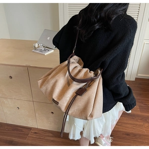 Detail of a large khaki pleated tote bag featuring long tassels and a brown leather handle