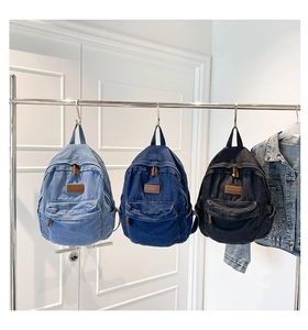 Three vintage denim backpacks in blue and black colors hanging on a metal rack