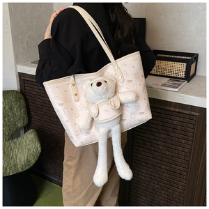 Detail of cute cream tote bag featuring brown cartoon bear prints and a plush bear pendant