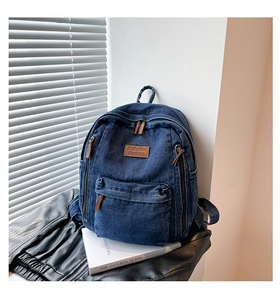 Detailed close-up of durable denim backpack with brown leather zip pulls and patch