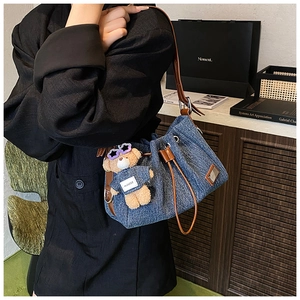Detail of blue denim bucket bag with brown leather strap and plush bear charm