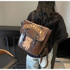 Detail of vintage brown leather backpack with holiday embroidery and teddy bear patch