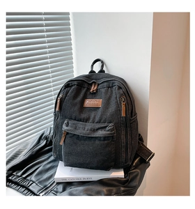 Detail of black canvas backpack featuring brown leather zipper pulls and round logo patch