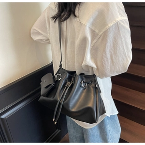 Side view of black matte leather drawstring bucket bag with silver ring detail and mini pouch