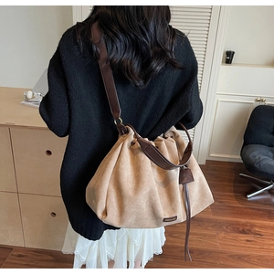 Detail of khaki pleated tote bag with dark brown leather straps and metal logo plate