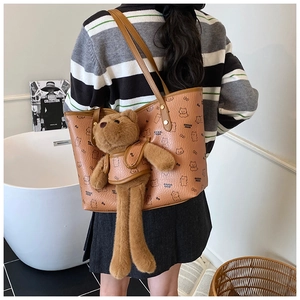 Detail of a brown lychee leather tote bag with cartoon bears and a large plush bear charm