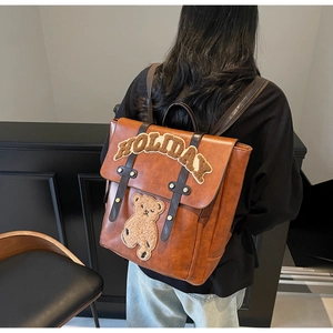 Detailed close-up of brown vintage leather backpack with plush bear embroidery
